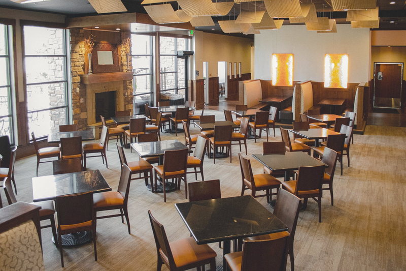 The main Elements dining room looking toward the window wall, with a dark ceiling grid, warm walls and wood chairs.