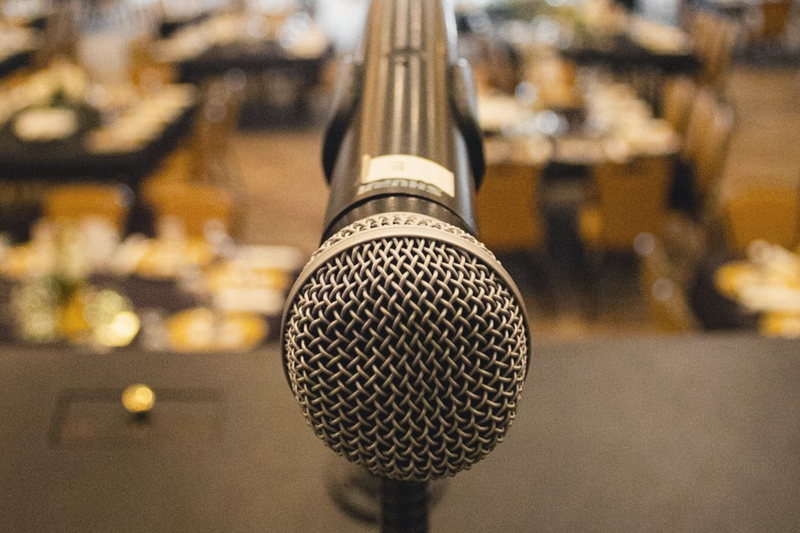 A microphone in sharp focus with a fully set ballroom dissolved to soft focus behind it.