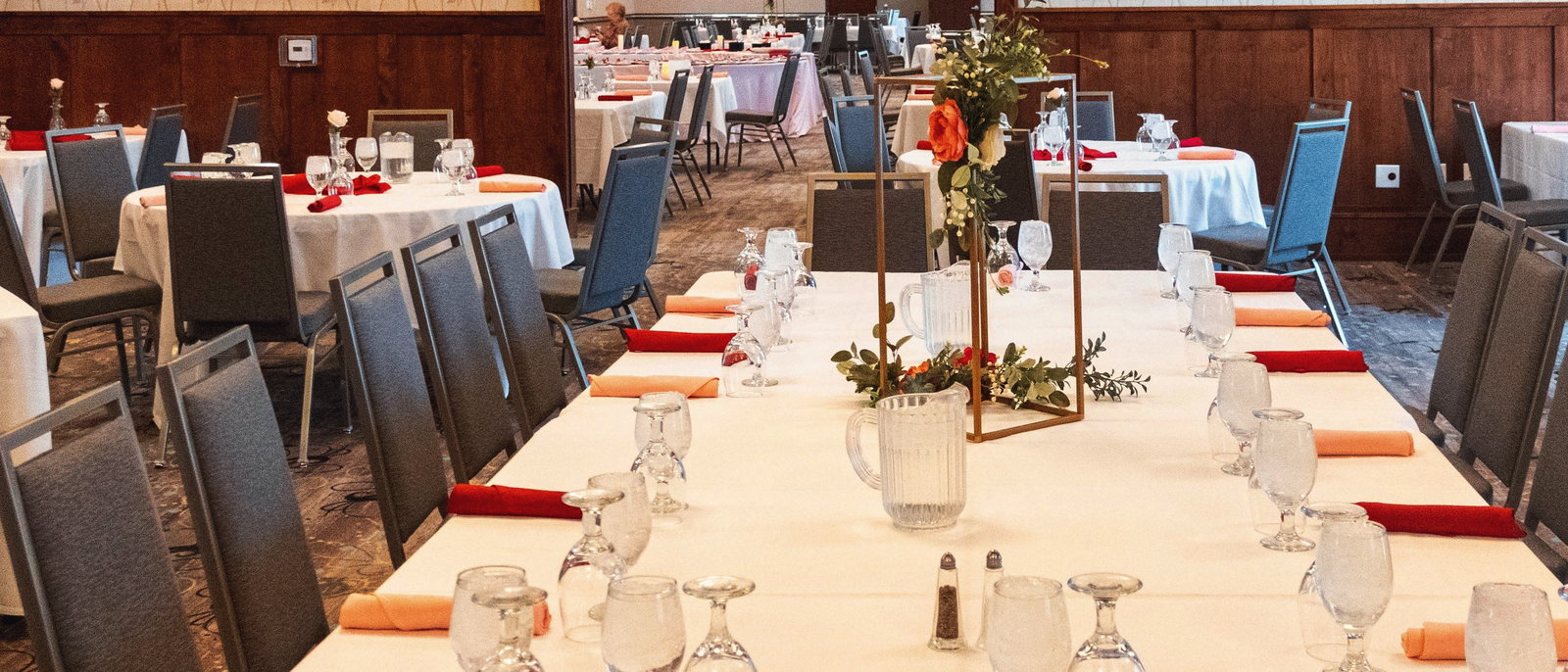 A long wedding head table dressed with gold candelabra and low floral runners, set for a reception.