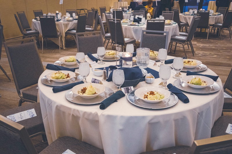 A round banquet table set with the first course plated, lit for a gala dinner.