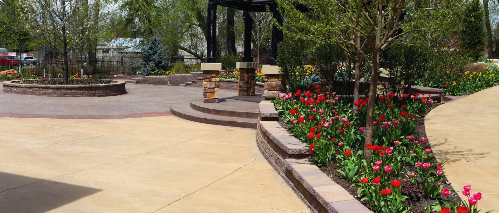 The Birch Courtyard at The Riverwoods, with stamped paving, a dark metal gazebo and beds of tulips in flower.