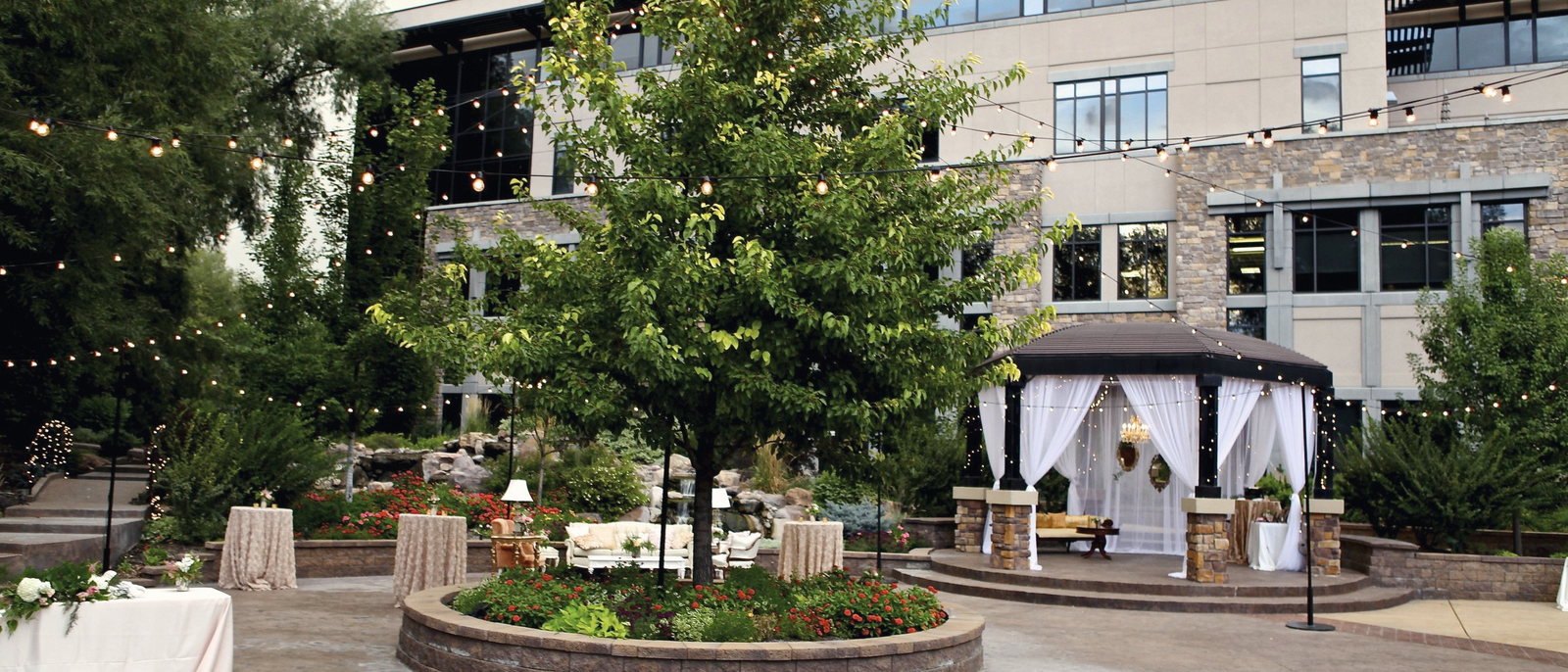 The courtyard at The Riverwoods set for an outdoor reception, with a draped gazebo, lounge furniture and strings of lights.