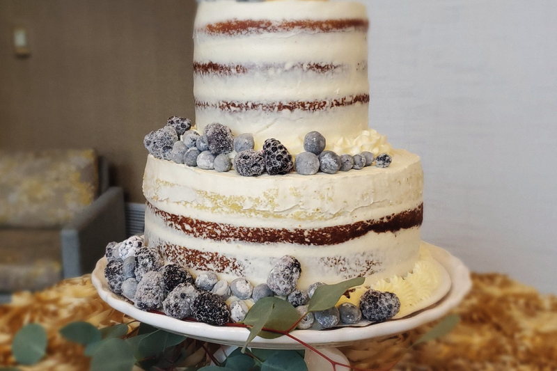 A naked tiered wedding cake dressed with fresh berries and eucalyptus.